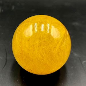 May include: A yellow crystal sphere with golden inclusions. The sphere is smooth and polished, with a high gloss finish.