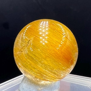 May include: A golden sphere with a striated, translucent surface. The sphere is made of natural crystal and has a warm, yellow hue.