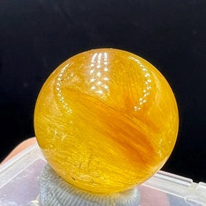 May include: A large, yellow, spherical crystal with a swirling, striated pattern. The crystal is smooth and polished.
