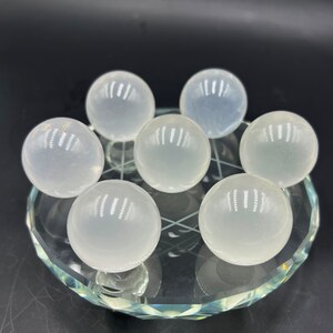 May include: Seven clear, smooth, white crystal spheres arranged in a circular pattern on a glass display stand.