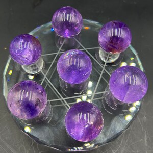May include: Seven amethyst spheres arranged in a circle on a clear glass base. The spheres are all the same size and are a deep purple colour.