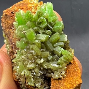 May include: A cluster of green and brown crystals on a brown matrix. The crystals are sharp and pointed, and they are arranged in a random pattern. The matrix is rough and textured.