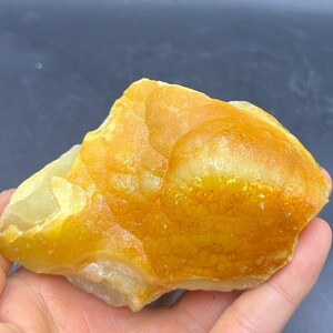 May include: A rough, natural stone with a mix of yellow and orange hues. The stone has a textured surface and irregular shape, with areas of lighter and darker coloration. The overall appearance suggests a mineral specimen or a decorative piece.