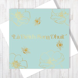 May include: A light blue card with gold foil accents. The card features a floral design with bees and the text "Lá Breith Sona Duit" in gold foil.