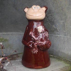 Könnte beinhalten: Eine braune Keramik-Affenfigur, die eine kleinere braune Keramik-Affenfigur hält. Der größere Affe hat ein lächelndes Gesicht mit braunen Augen und einer braunen Nase.