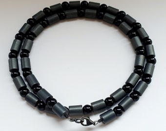 Könnte beinhalten: Eine schwarze und graue Perlenkette mit einem silbernen Verschluss. Die Kette besteht aus runden Perlen und ist etwa 50 cm lang.