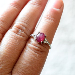 Peut inclure: Une bague en argent avec une grande pierre de rubis ovale et de plus petites pierres blanches sur la bande.