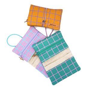 Peut inclure: Trois pochettes rectangulaires en tissu avec des motifs à carreaux. L'une est orange avec des lignes violettes, une est violet clair avec des lignes bleues, et une est bleu sarcelle avec des lignes roses. Chaque pochette a une fermeture éclair.