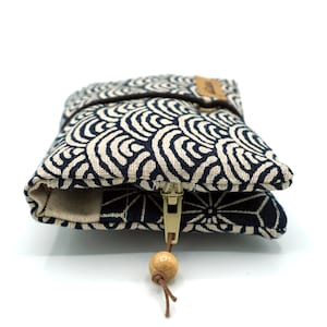 May include: A small, zippered pouch with a blue and white wave pattern. The pouch has a wooden bead on the zipper pull.
