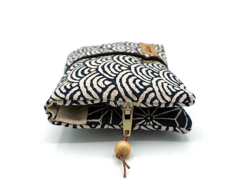 May include: A small, zippered pouch with a blue and white wave pattern. The pouch has a wooden bead on the zipper pull.