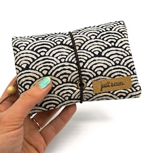 May include: A small, blue and white fabric pouch with a wave pattern. The pouch has a brown leather label that says "just sewn".