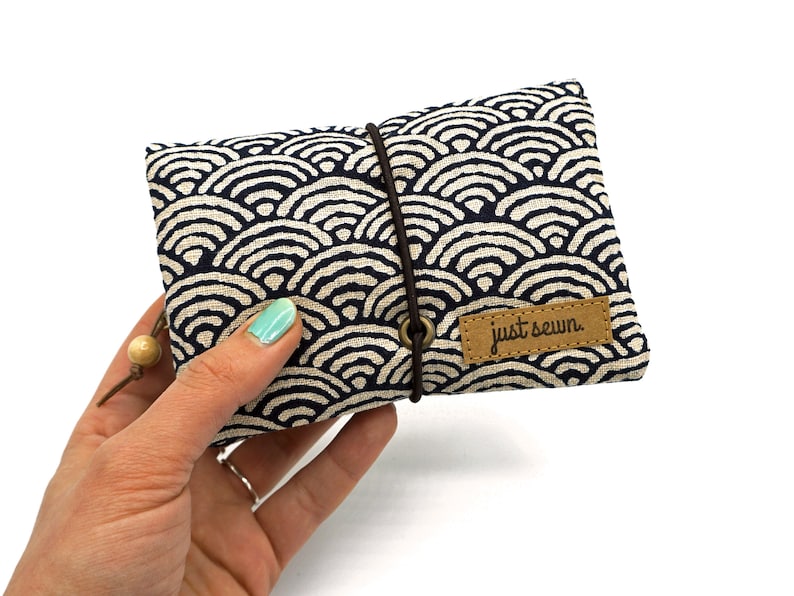 May include: A small, blue and white fabric pouch with a wave pattern. The pouch has a brown leather label that says "just sewn".