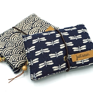 May include: Two small fabric pouches with zipper closures. One pouch is blue with a white dragonfly pattern and the text "just sewn". The other pouch is beige with a blue wave pattern.
