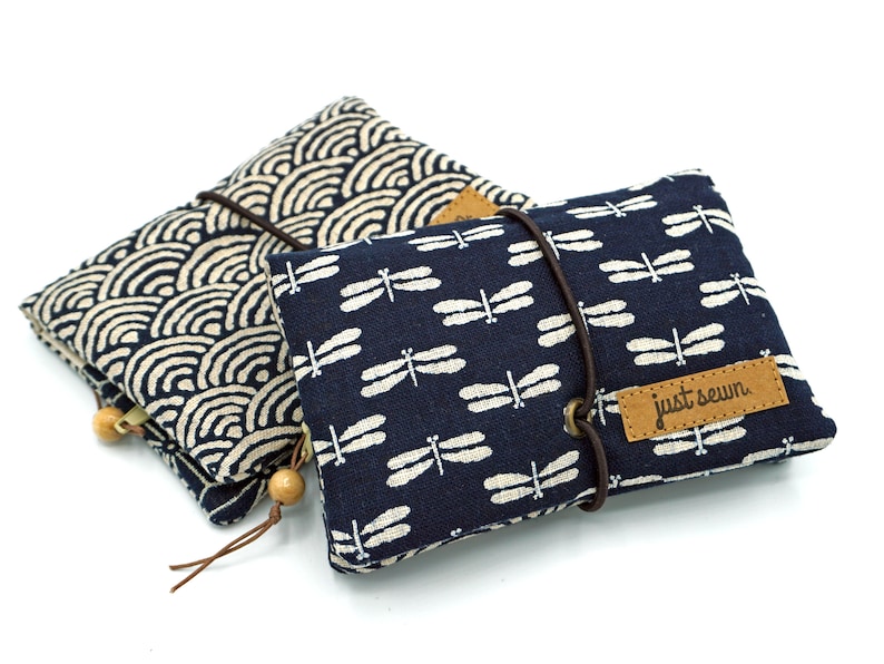 May include: Two small fabric pouches with zipper closures. One pouch is blue with a white dragonfly pattern and the text "just sewn". The other pouch is beige with a blue wave pattern.