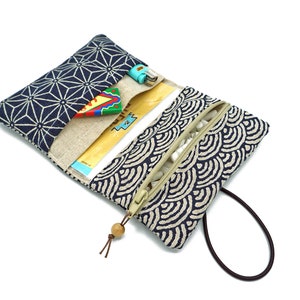 May include: A blue and white patterned fabric pouch with a zipper closure and a brown strap. The pouch is open and has a small, colorful toy inside.