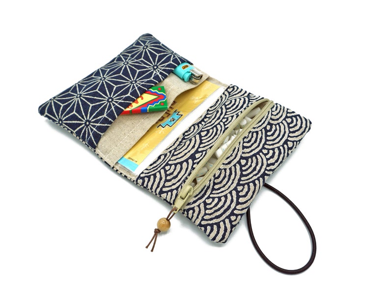 May include: A blue and white patterned fabric pouch with a zipper closure and a brown strap. The pouch is open and has a small, colorful toy inside.