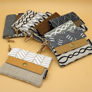 Può includere: Una collezione di piccole pochette in tessuto con vari motivi e colori. Le pochette presentano una chiusura a patta con bottone e un accento in pelle. I design includono forme geometriche, linee ondulate e motivi strutturati.