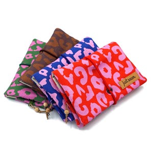 Peut inclure: Quatre pochettes en tissu aux motifs variés : vert à fleurs roses, marron à pois marron, bleu à pois roses et rouge à pois roses. Chaque pochette est fermée par un cordon avec une perle en bois. La pochette rouge porte l'étiquette "just sewn".