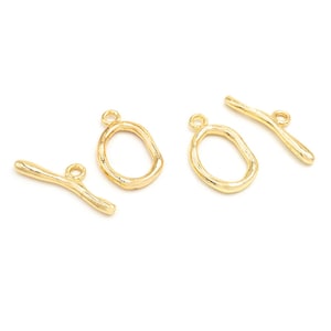 Pode incluir: Fecho de correr de metal dourado com duas alças ovais e um conector de barra reta. O fecho é projetado para a fabricação de joias e artesanato.