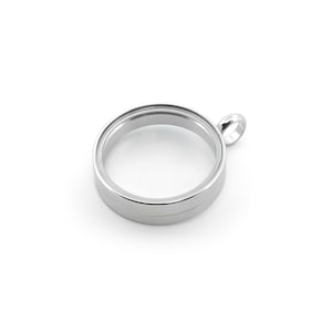 Op de afbeelding: Een cirkelvormige zilverkleurige metalen medaillonhanger met een hol midden en een gladde, gepolijste afwerking. Het medaillon is voorzien van een klein, geïntegreerd cirkelvormig oogje aan de bovenkant voor bevestiging met een strak oppervlak.