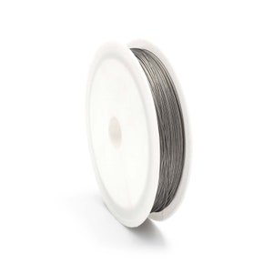 Può includere: Una bobina di filo grigio, avvolta strettamente su una bobina di plastica bianca. Il filo sembra essere di metallo ed è ordinatamente organizzato. La bobina è angolata, mostrando la consistenza e la forma del filo.