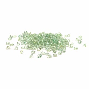 Op de afbeelding: Een hoop kleine, lichtgroene edelstenen verspreid over een witte achtergrond.