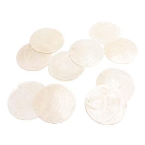 Könnte beinhalten: Zehn cremefarbene, runde Scheiben, die an Muscheln erinnern, mit kleinen Löchern am Rand. Sie haben einen perlmuttartigen Glanz und liegen auf weißem Hintergrund. Geeignet für Schmuckherstellung oder Bastelprojekte. Jeder Kreis hat einen Durchmesser von etwa 3 cm.