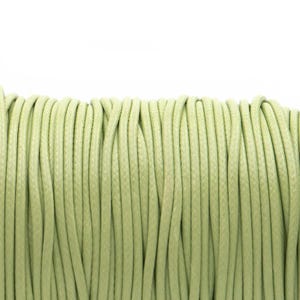 Può includere: Primo piano di una bobina di cordoncino verde chiaro. Il cordoncino è avvolto strettamente, con ogni filo visibile e parallelo agli altri. Il colore è un verde tenue e smorzato, e la consistenza appare liscia. Lo sfondo è bianco.