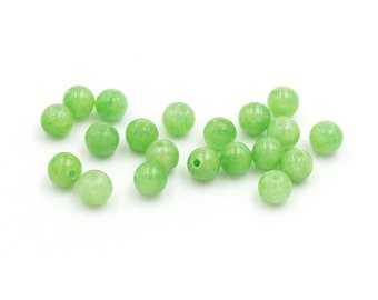 Op de afbeelding: Een strooiing van gladde, ronde, lichtgroene jade kralen. De kralen zijn allemaal ongeveer even groot en hebben een licht doorschijnende uitstraling.
