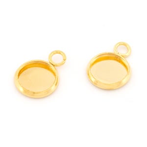Peut inclure: Deux breloques pendantes en métal doré avec un sertissage rond pour une pierre de cabochon. Chaque breloque a un anneau de saut pour l'attacher à une chaîne ou un cordon.