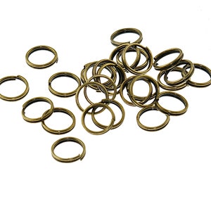 Op de afbeelding: Een stapel van 20 gouden metalen sleutelringen. De sleutelringen zijn allemaal even groot en even gevormd, en ze zijn in een willekeurig patroon gerangschikt.