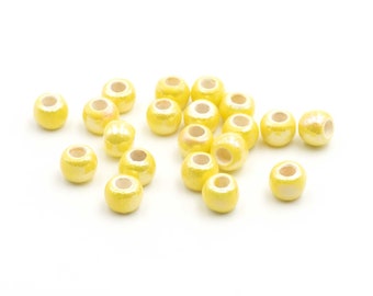 May include: A group of yellow beads with a pearlescent finish. The beads are scattered on a white surface.
