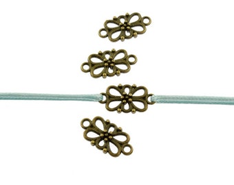 Puede incluir: Cuatro abalorios de metal de color dorado antiguo en forma de flor con un diseño decorativo. Los abalorios están enhebrados en una cinta azul claro.