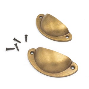 Peut inclure: Deux poignées en forme de coupe de couleur laiton antique avec des vis assorties. Les poignées ont une forme en demi-lune avec deux trous de vis à chaque extrémité. Les vis sont noires et assorties aux poignées. Idéal pour les armoires et les tiroirs.
