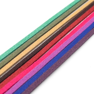 Può includere: Una collezione di strisce di pelle scamosciata colorate in varie tonalità, tra cui verde, beige, rosso, rosa, viola e blu. Le strisce sono disposte diagonalmente su uno sfondo bianco, mostrando la loro consistenza e le variazioni di colore. Ideali per progetti creativi.