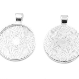 Puede incluir: Dos bandejas de colgantes plateadas con un diseño circular texturizado. Las bandejas tienen un bucle en la parte superior para sujetar una cadena o un cordón.