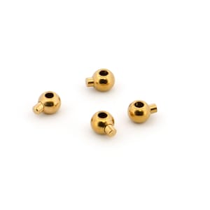 Può includere: Quattro piccole perline metalliche sferiche color oro, ciascuna caratterizzata da una superficie liscia e lucida e da una singola sporgenza cilindrica su un lato. Ogni perlina presenta un'apertura circolare centrale, creando una forma cava.