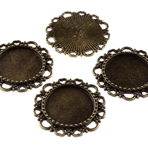 May include: Four antique bronze-coloured metal frames with a heart-shaped design. The frames are designed to hold round glass or plastic cabochons.