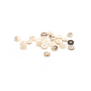 Könnte beinhalten: Eine Sammlung von weißen und braunen Muschelkernperlen in Ringform. Die Perlen sind auf einer weißen Oberfläche verstreut.
