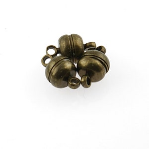 May include: Three antique gold magnetic clasps for jewelry making. Each clasp has a round shape with a grooved design and a small loop for attaching to a necklace or bracelet.