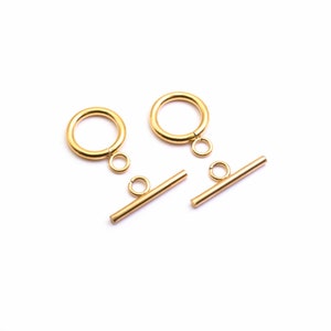 May include: Two sets of gold-colored toggle clasps, each consisting of a ring and a bar. The ring has a small loop attached, and the bar has a similar loop. The clasps are displayed on a white background, showcasing their shiny, metallic finish.