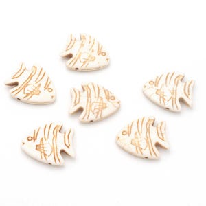 Könnte beinhalten: Sechs cremefarbene, fischförmige Perlen mit braunen, geätzten Details. Jede Perle hat ein kleines Loch zum Auffädeln. Die Fische haben ein stilisiertes Design mit Flossen und Schuppen. Geeignet für Schmuckherstellung oder Bastelprojekte.