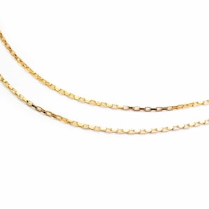 Peut inclure: Deux fines colliers en chaîne dorée avec un design à maillons rectangulaires. Les chaînes sont présentées sur un fond blanc, soulignant leurs détails fins et leur couleur chaude. Les chaînes sont légèrement incurvées, suggérant leur flexibilité.