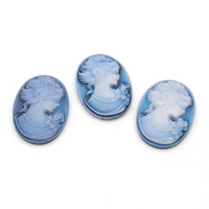 Könnte beinhalten: Drei ovale Cameo-Anhänger in Hellblau und Weiß. Jeder Anhänger zeigt das Profil einer Frau mit detaillierten Haaren und einer Rose. Die Cameos sind vor einem hellblauen Hintergrund platziert.