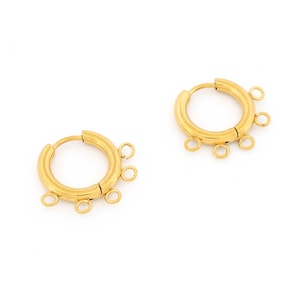 Peut inclure: Une paire de boucles d'oreilles créoles dorées. Chaque boucle d'oreille a un design circulaire avec plusieurs petites boucles attachées sur le bord extérieur. Les boucles d'oreilles sont sur fond blanc.
