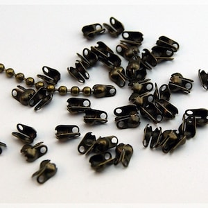 Könnte beinhalten: Eine Gruppe antiker goldfarbener Metallverschlüsse für die Schmuckherstellung. Die Verschlüsse sind klein und haben eine abgerundete Form mit zwei Schlaufen auf jeder Seite.