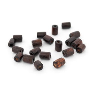 以下が含まれることがあります： 白い面に散らばる濃い茶色の木製ビーズのコレクション。ビーズは円筒形で、中央に穴があり、木目が現れています。ジュエリー作りや工芸品に適しています。