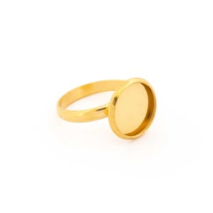 Peut inclure: Une bague dorée avec un sertissage de lunette rond. L'anneau est fin et lisse, menant à un sertissage circulaire conçu pour contenir une pierre ou un autre ornement. La bague est présentée sur un fond blanc.