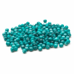 Op de afbeelding: Een stapel teal blauwe glazen kralen met witte marmering. De kralen zijn rond en hebben een gladde, glanzende afwerking.