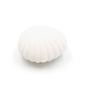 Peut inclure: Une boîte à bijoux blanche en forme de coquillage. La boîte a une surface texturée et nervurée et une forme arrondie, ressemblant à une coquille Saint-Jacques. La boîte à bijoux est faite d'un matériau doux et mat.